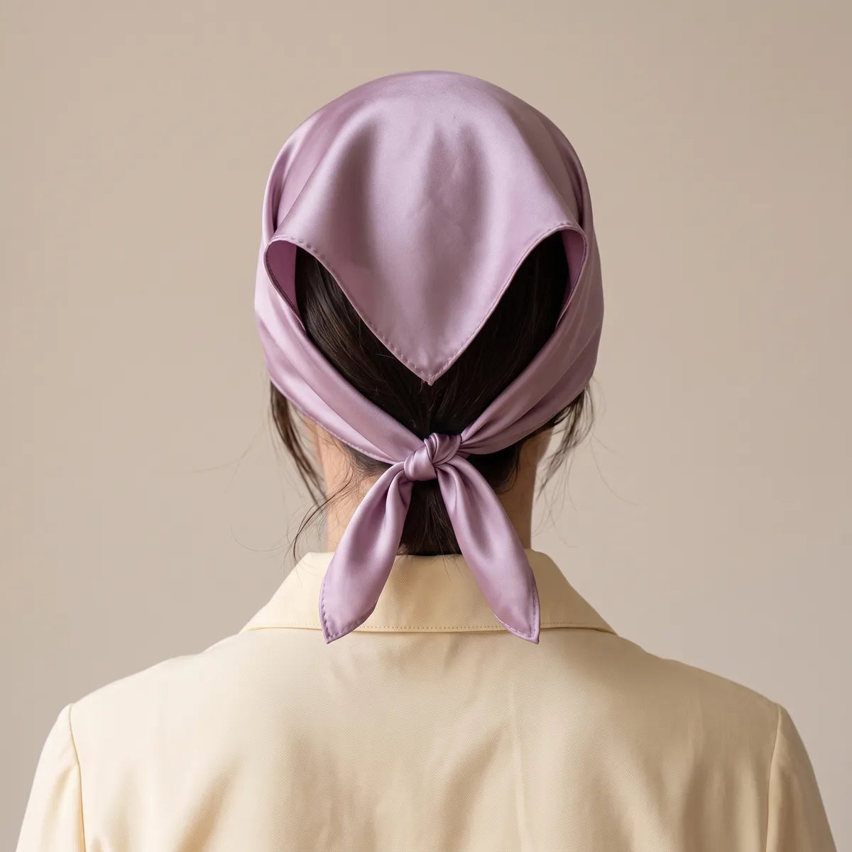 Lilac silk bandana from the back, covering the hair and knotted at the nape over a cream jacket