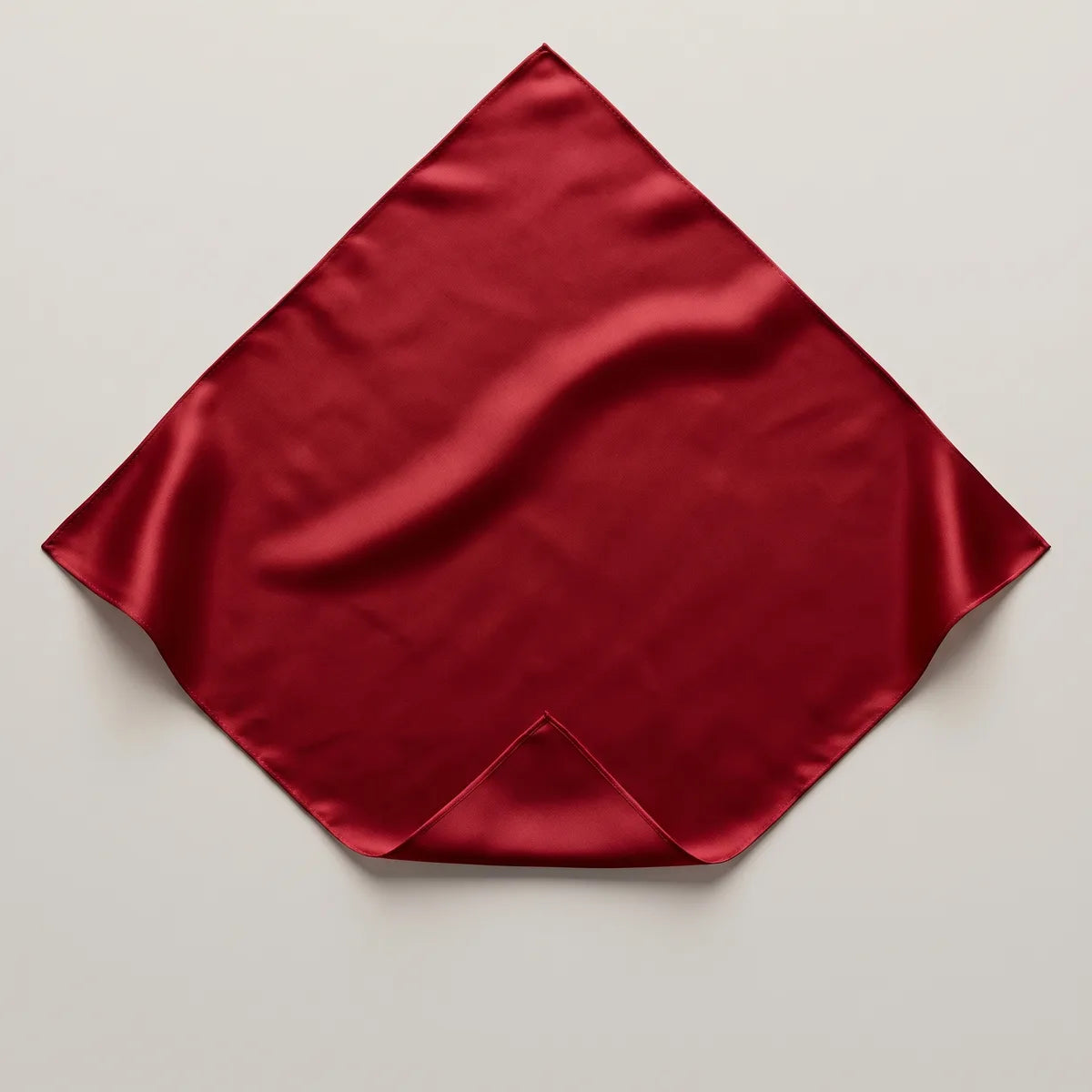 Solid red silk bandana lying flat, a deep cherry square with one corner folded back