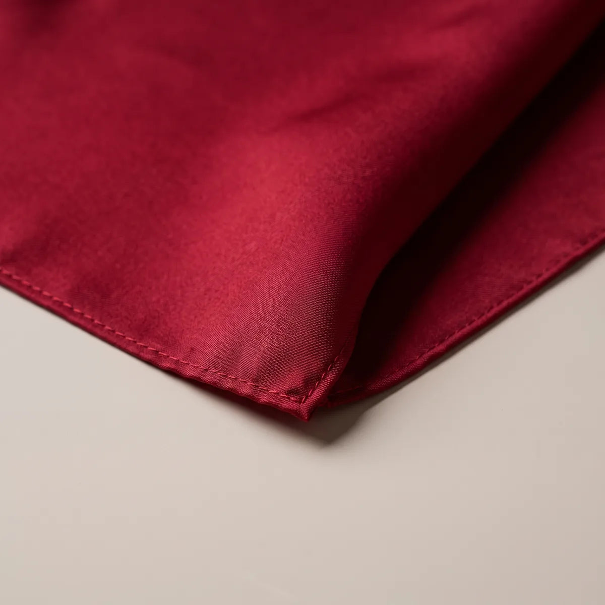 Corner of the solid red bandana up close, the stitched hem in the same cherry red