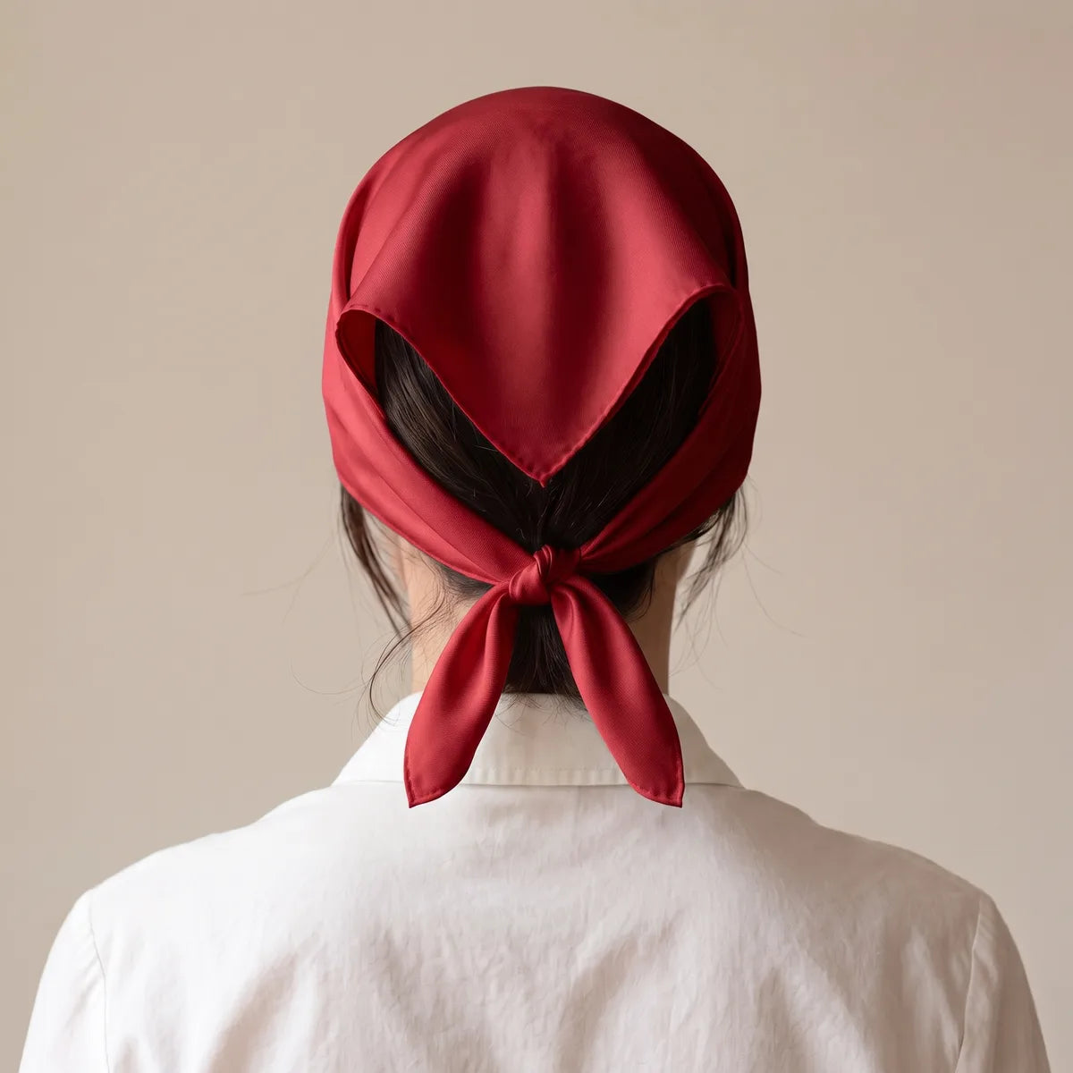 Back view of a cherry red silk bandana over the hair, ends tied together at the nape