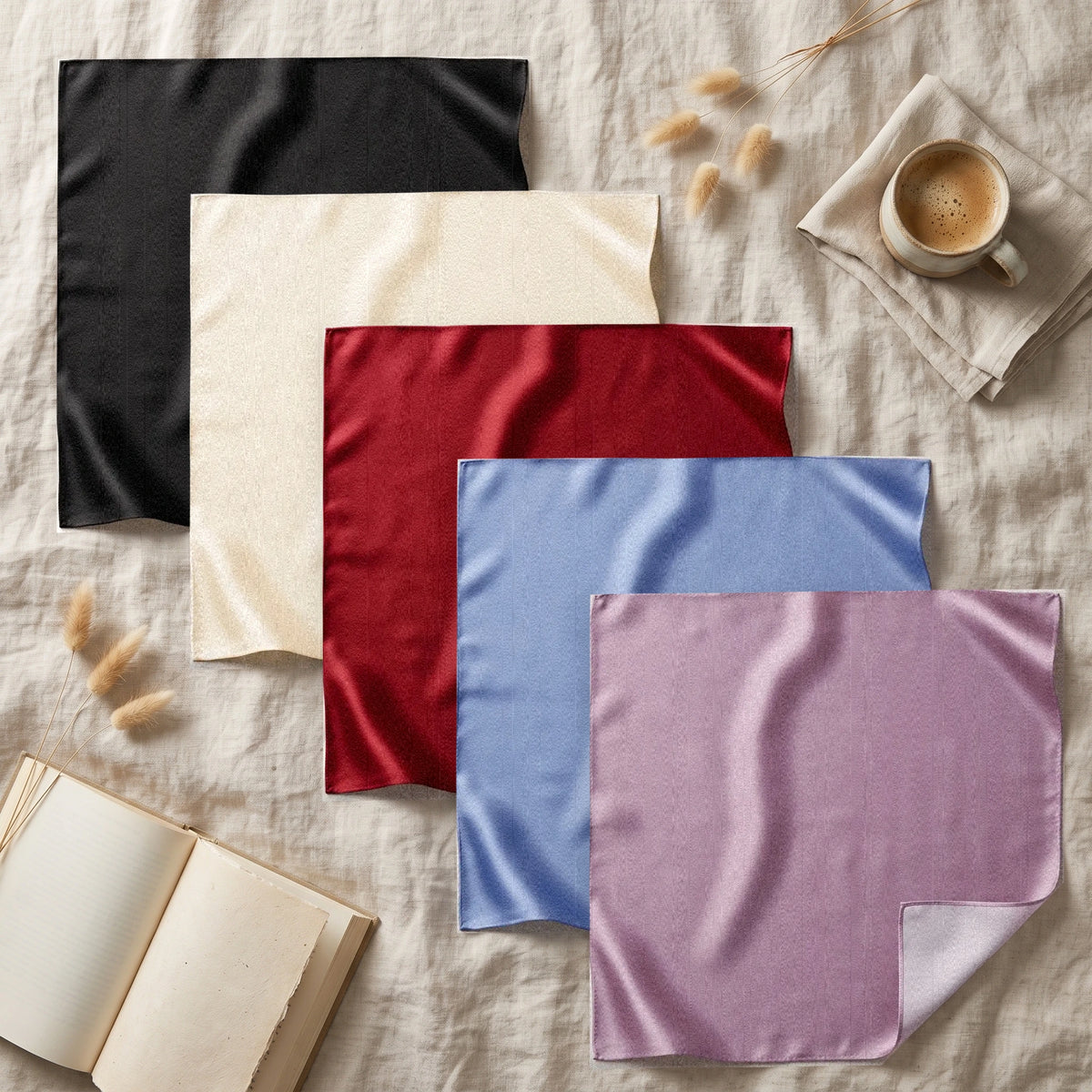 Black, cream, red, blue and lilac bandanas fanned out on linen with a book and a coffee cup