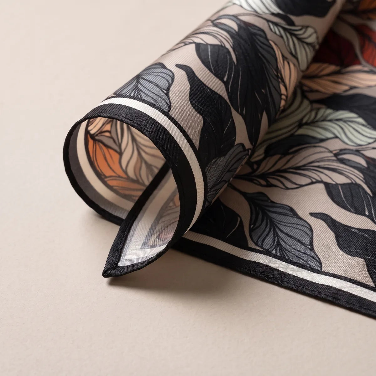 Rolled corner of the leaf scarf: black edge, cream stripe and black and gray leaves