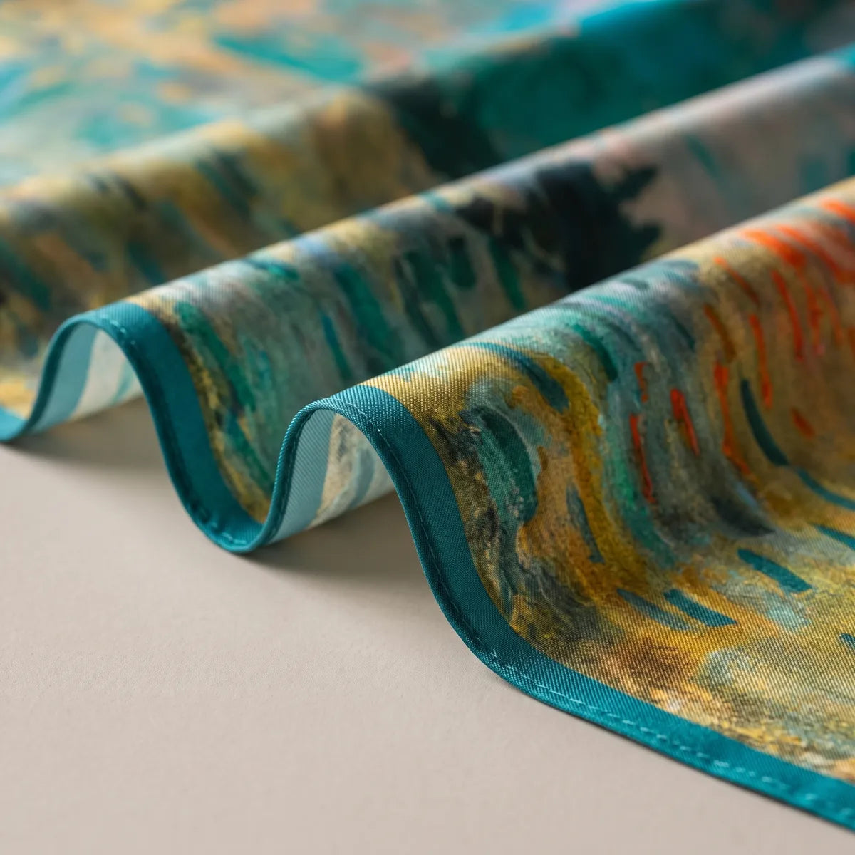 Detail of the teal edge on the Monet silk bandana, with ochre, teal and orange-red brushstrokes in folds