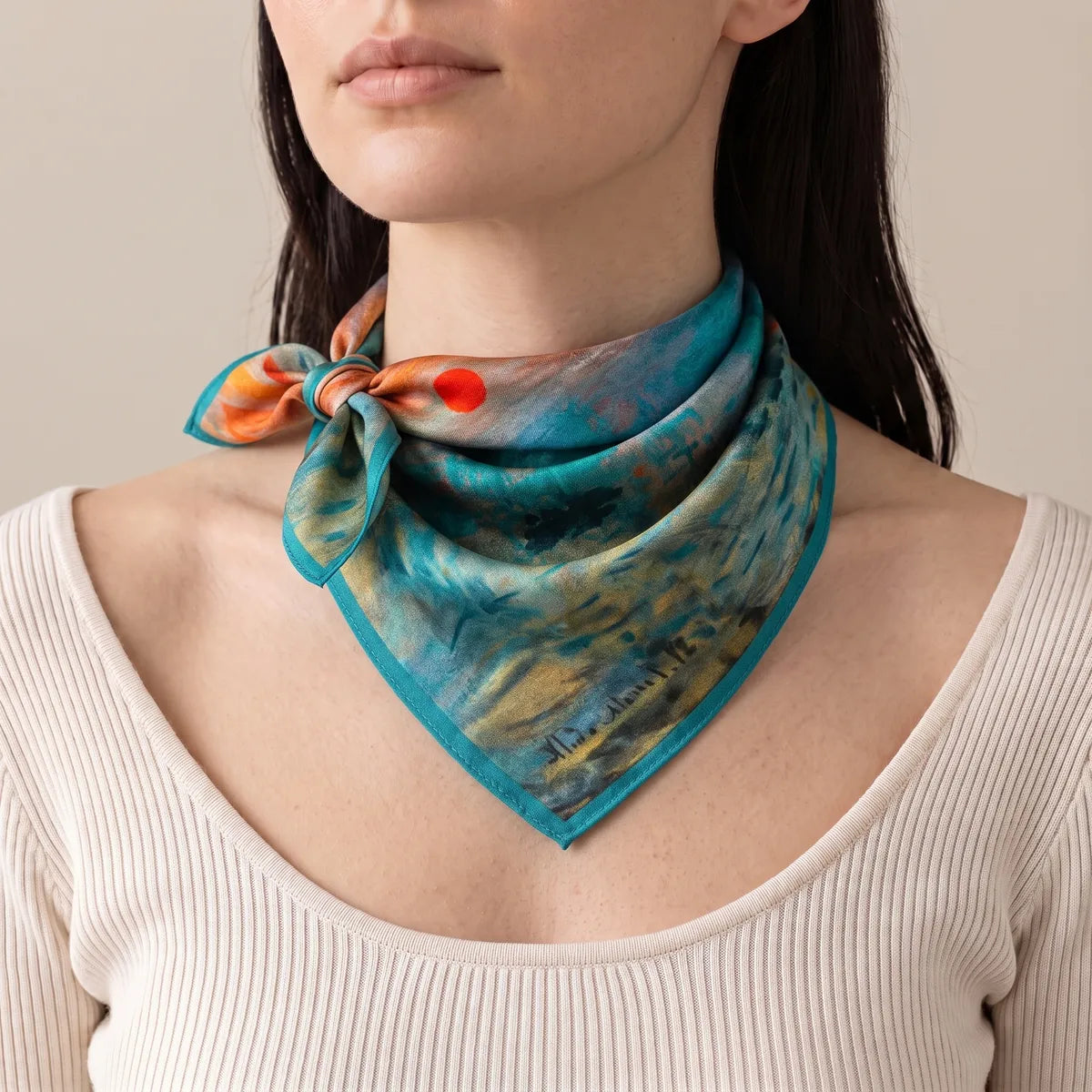 Woman in a cream ribbed top wearing the teal Monet silk bandana with a side knot, the red sun beside the knot