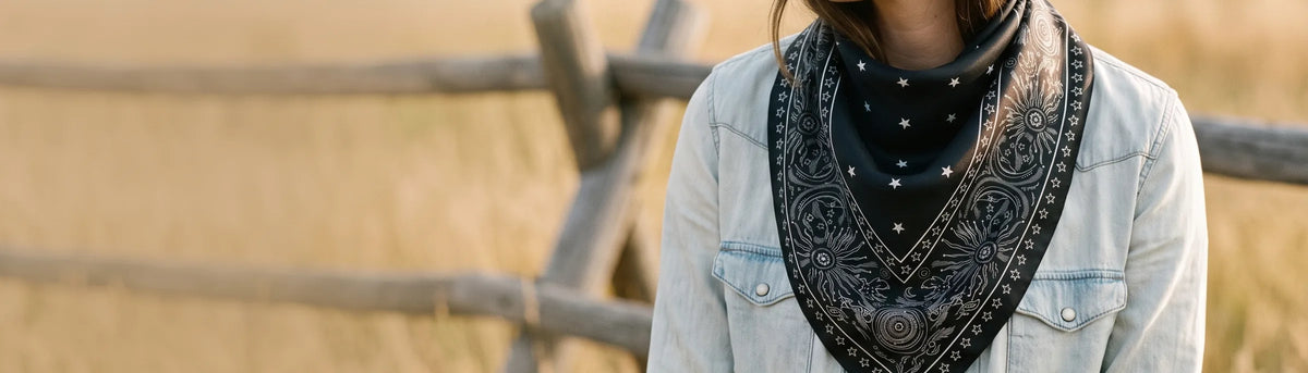 Black star print silk bandana worn point front with a denim jacket by a ranch fence