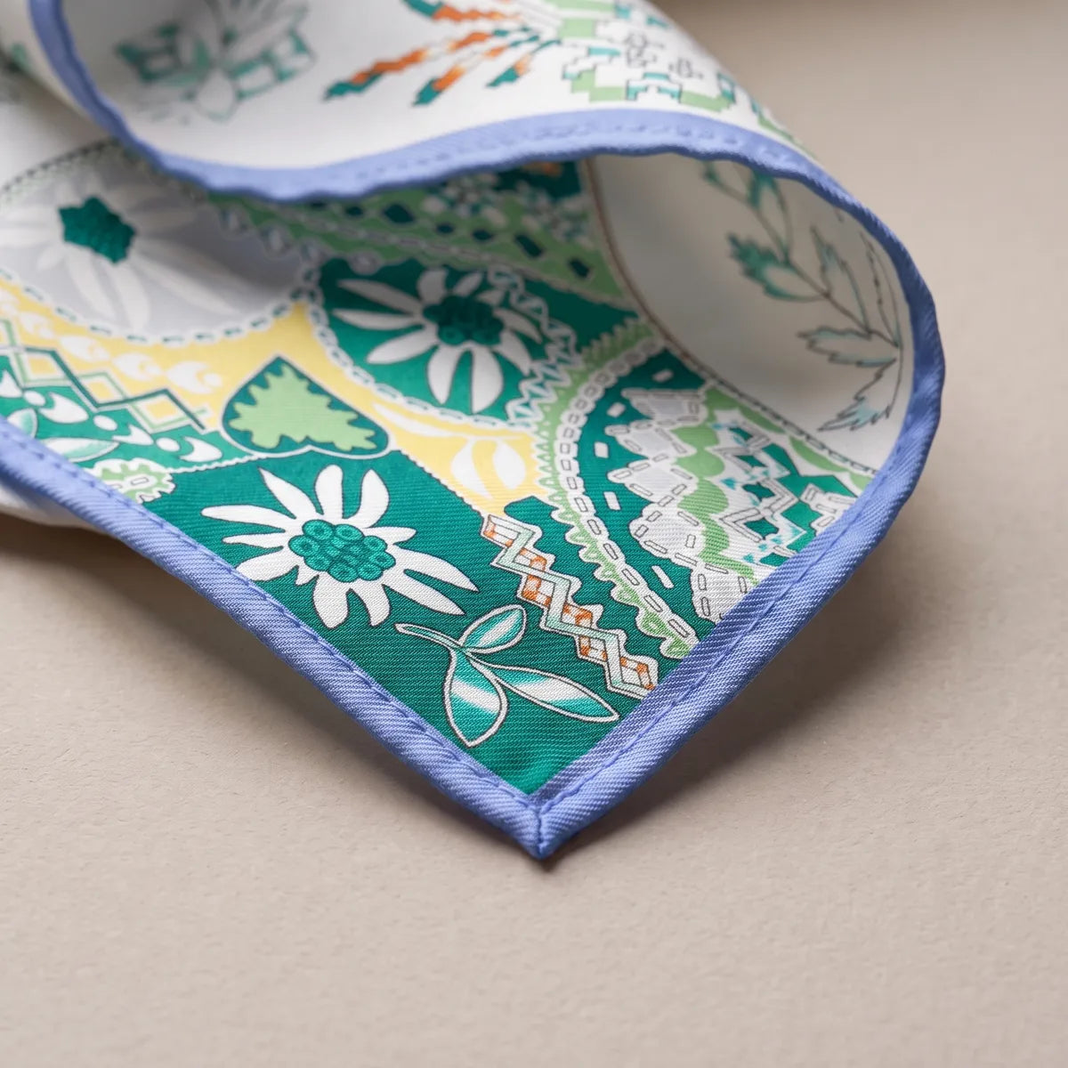 Corner of the white shawl: teal patches with daisies and zigzags above a periwinkle hem