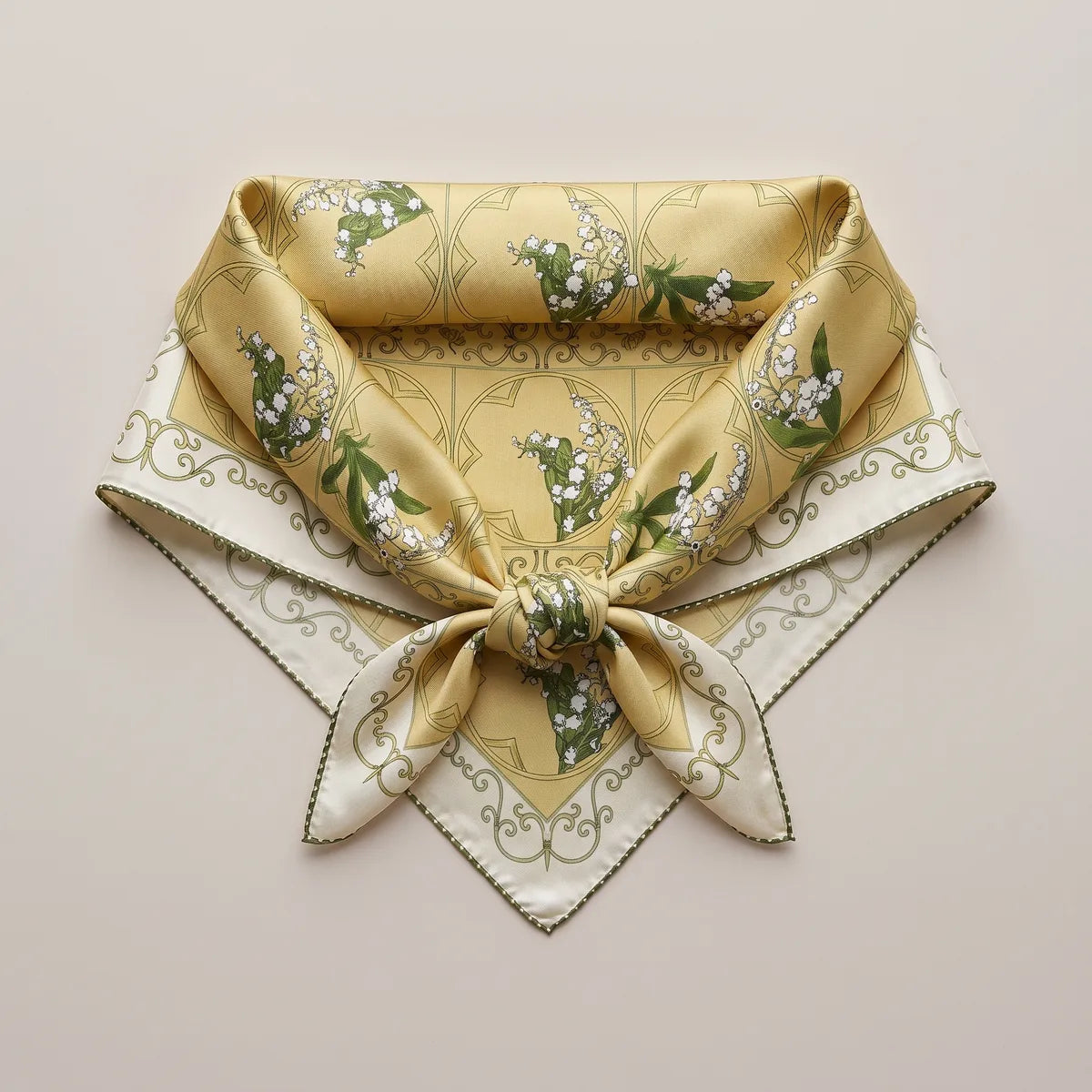 Butter yellow silk square knotted into a neckerchief shape and laid flat, lily sprigs above the knot