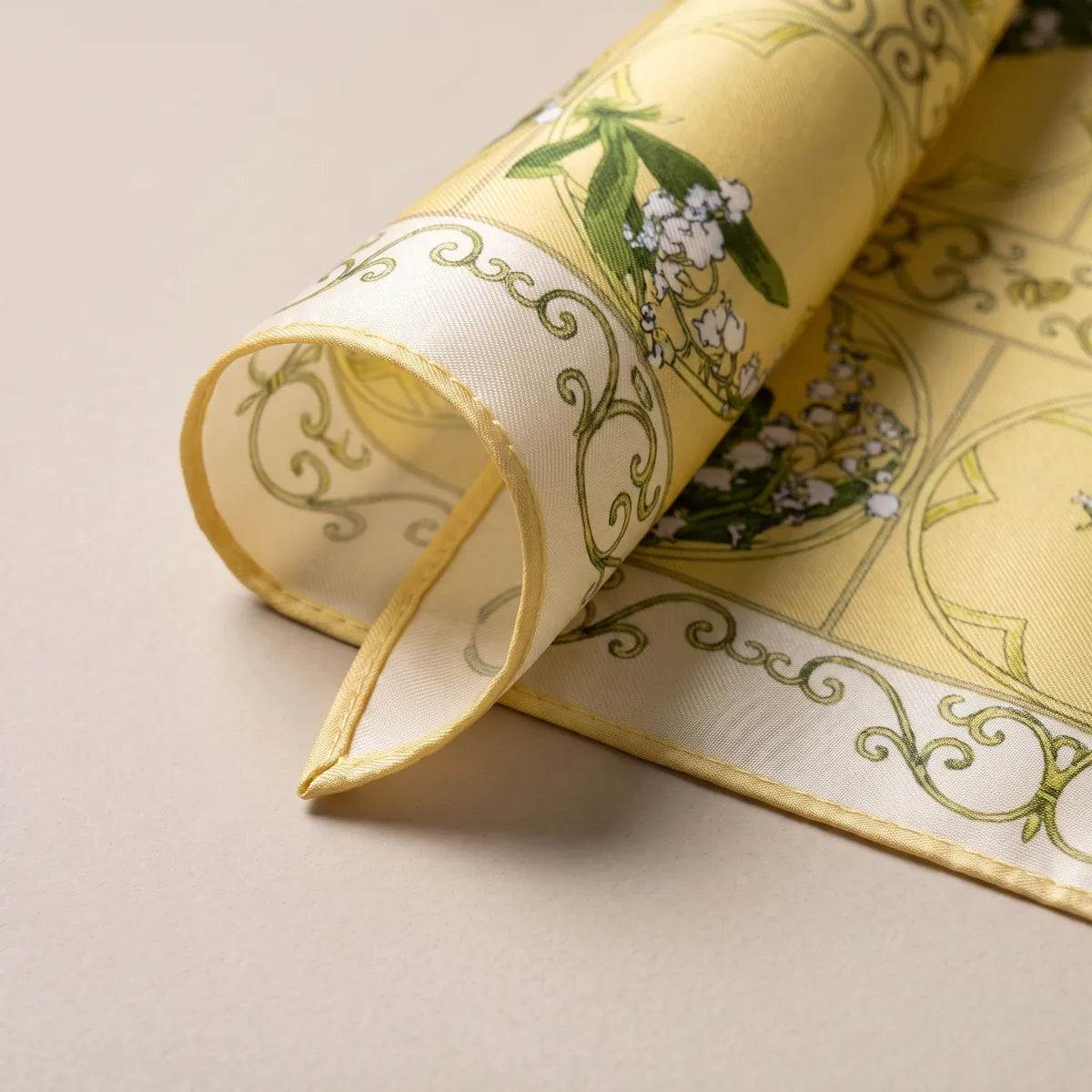 Corner of the yellow silk square curled over: a lily of the valley sprig, olive scrolls and the pale reverse